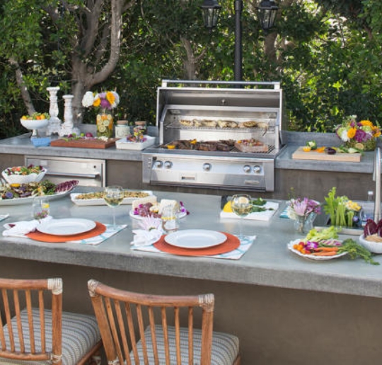 outdoor kitchen with table and chairs set for dinner from custom pool builders