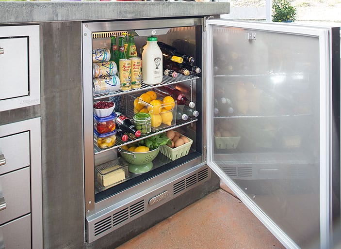 Outdoor under-counter refrigerator with glass door stocked with drinks, produce, and groceries